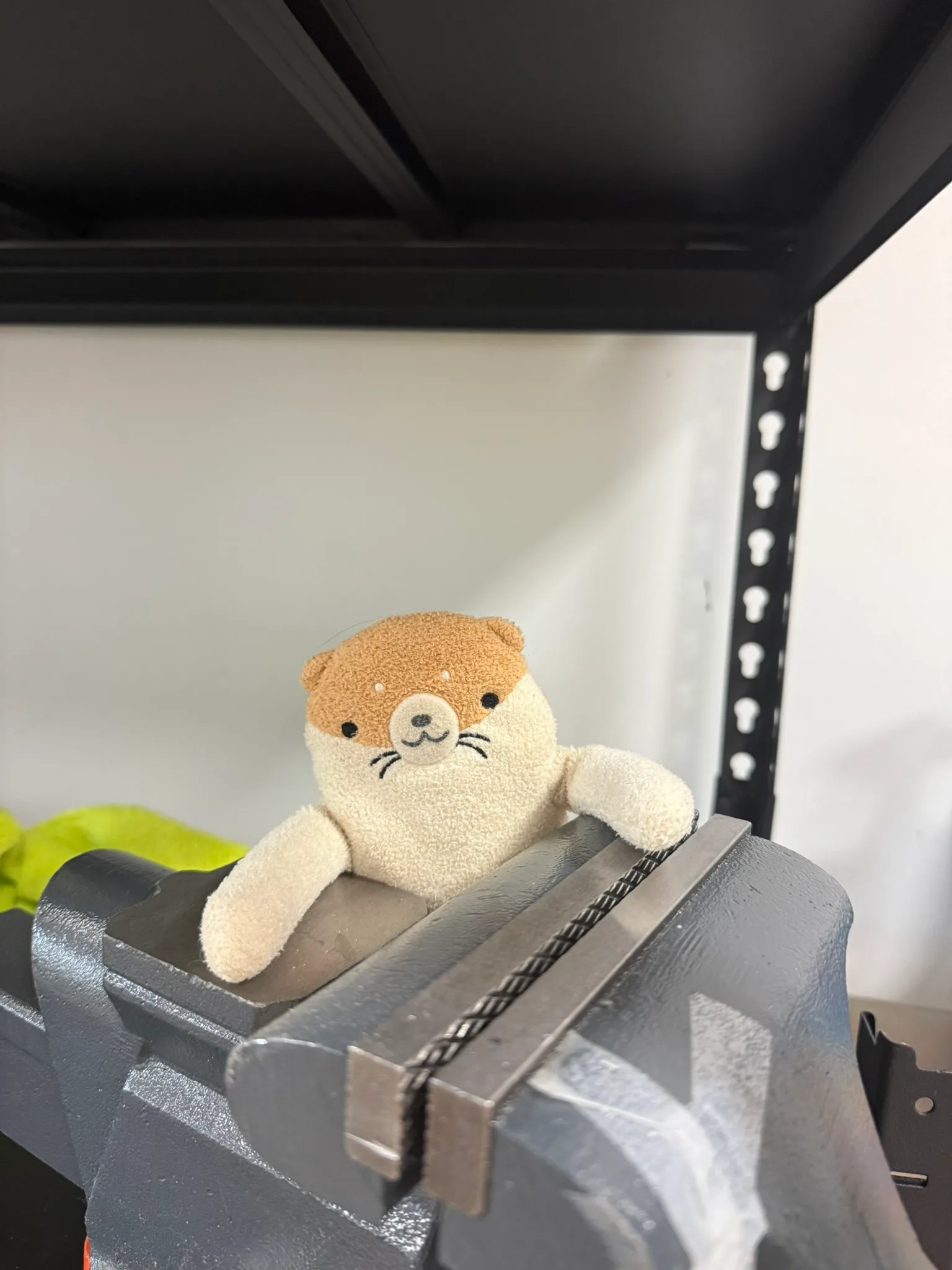 Rufus, a plush otter, leaning over a metalworking vise